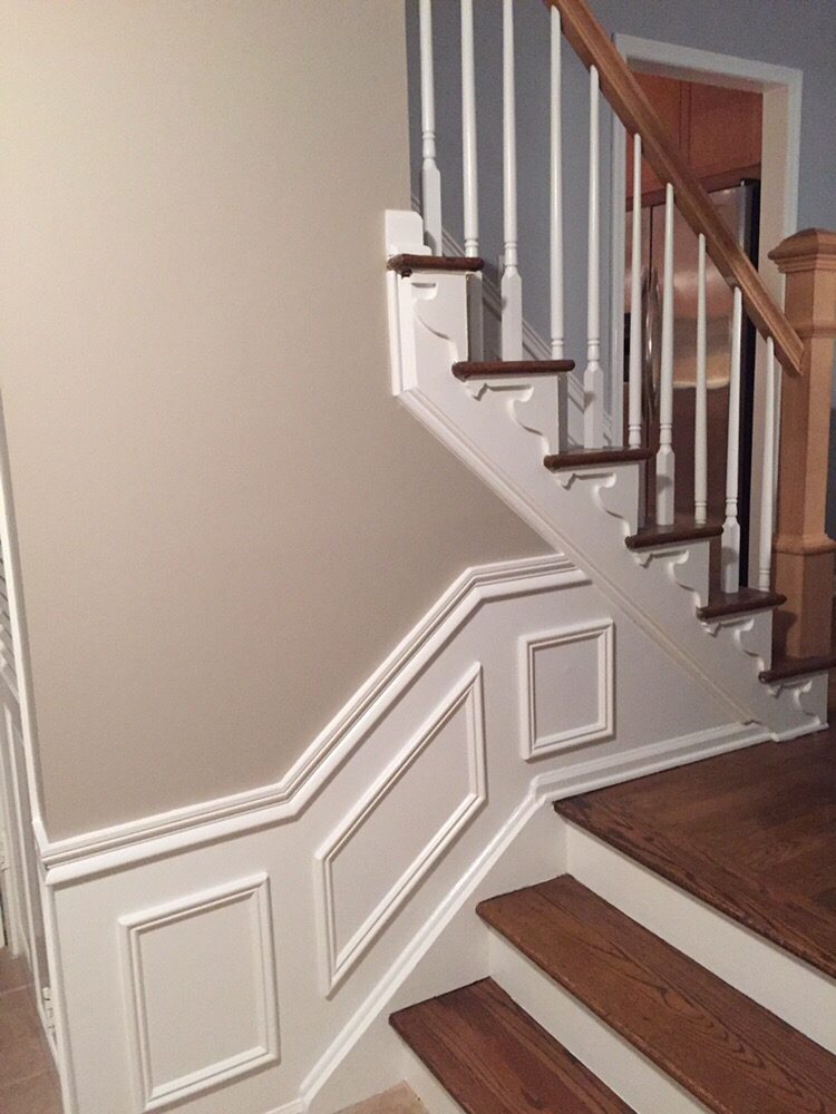 Repainted staircase with crisp white wainscoting, panel moulding, and neutral walls — fresh paint and sharp lines transform the entry.